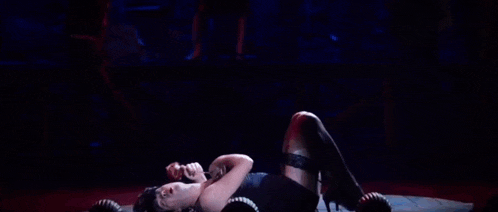a woman in a black dress and stockings is laying on the floor on a stage .