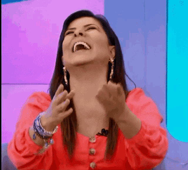 a woman in a red shirt and earrings is laughing with her mouth open .