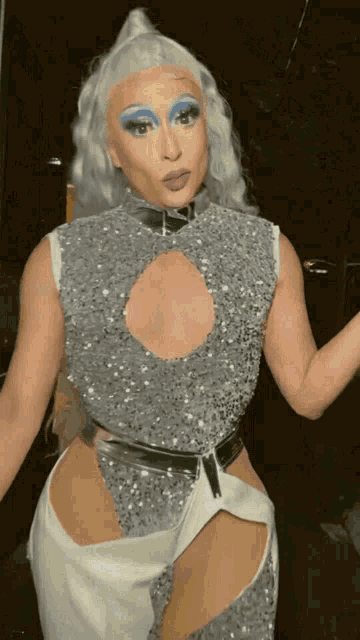 a woman with white hair and blue makeup is wearing a silver top