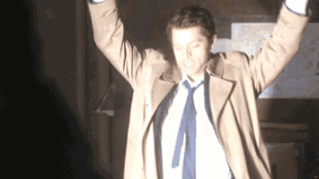 a man in a trench coat and tie is standing with his arms in the air