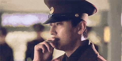 a man in a military uniform is smoking a cigarette and looking at something .