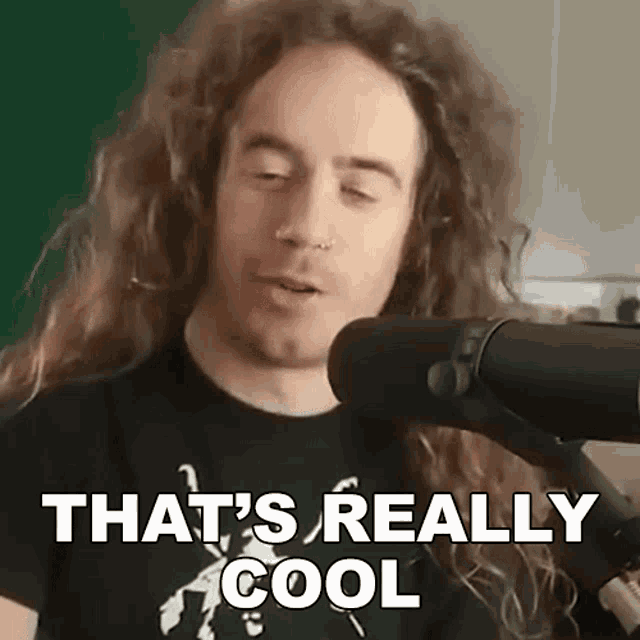 a man with long curly hair is standing in front of a microphone and says that 's really cool .