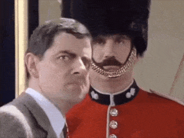 a man in a suit and tie is standing next to a man in a red uniform with a mustache .
