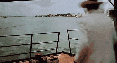 a man in a cowboy hat is standing on a boat looking out over a body of water