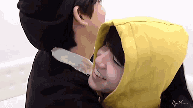 a man in a yellow hoodie is hugging another man in a black hat .