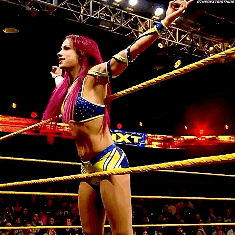 a woman with pink hair is standing in a wrestling ring with her arm outstretched .