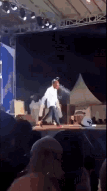 a man in a white shirt stands on a stage in front of a crowd