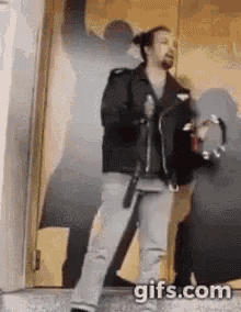 a man is standing in front of a door holding a tambourine and a gun .