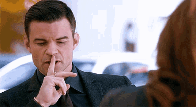 a man in a suit and tie is holding his finger to his mouth and talking to a woman .