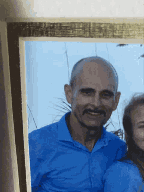 a man in a blue shirt with a mustache smiles for the camera