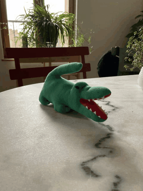 a green stuffed crocodile with red teeth is laying on a table