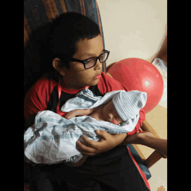 a boy with glasses is holding a baby in his lap