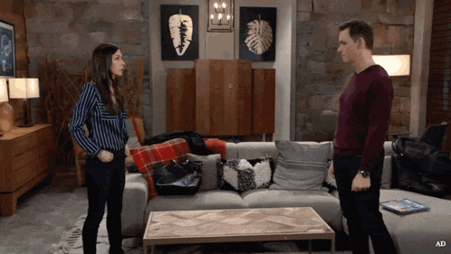 a man and a woman standing next to each other in a living room with an ad on the bottom right