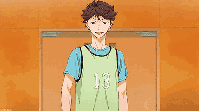 a man in a green jersey with the number 13 on it is holding a volleyball .