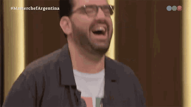 a man wearing glasses is laughing in front of a masterchef argentina logo