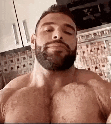 a shirtless man with a beard is taking a picture of his chest .