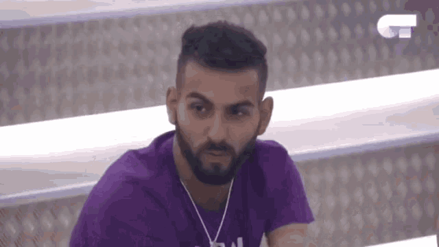 a man with a beard is wearing a purple shirt with the letter t on the front