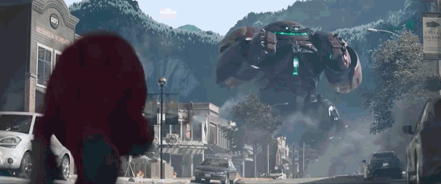 a giant robot is flying over a small town with cars parked on the side of the road .