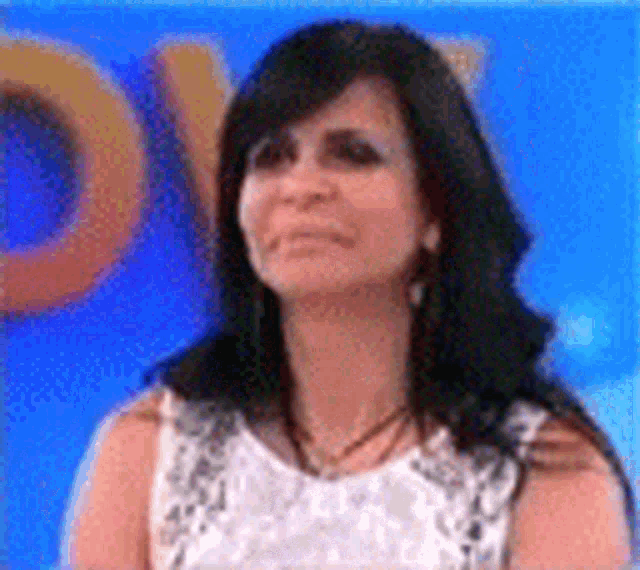a woman in a white dress is standing in front of a blue background and making a funny face .