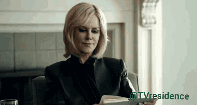a woman sits in a chair reading a book with a tv residence logo in the corner