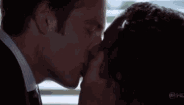 a man in a suit and tie is kissing another man on the nose .
