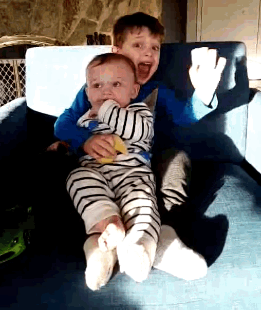 two young boys are sitting on a couch and one of them is holding a baby in his arms
