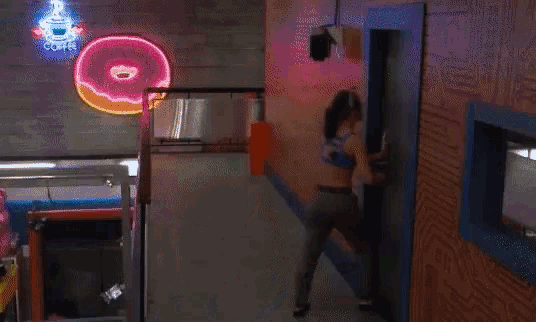a woman is standing in a hallway with a neon donut sign above her head