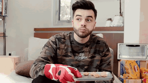 a man wearing a 100 thieves sweatshirt sits on a couch
