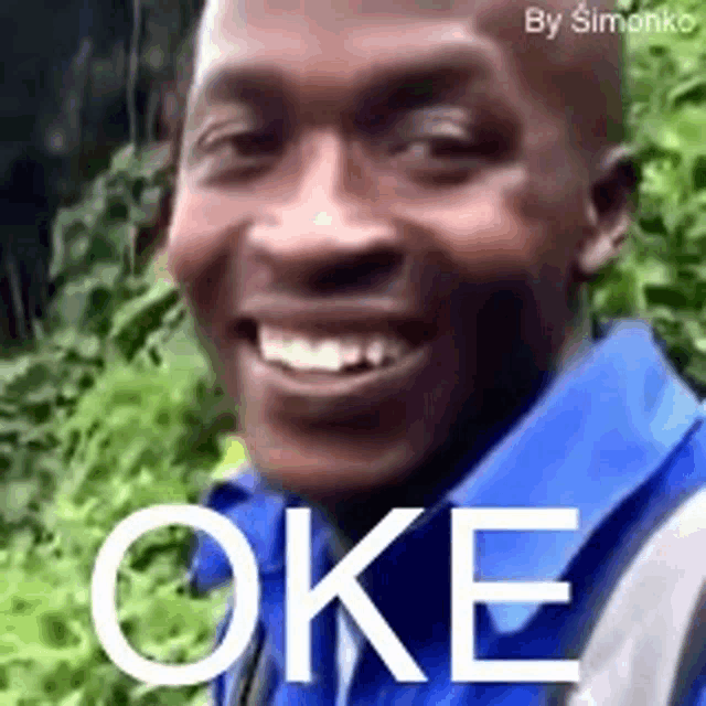 a man in a blue shirt is smiling and the word oke is on his face .