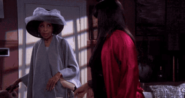 two women standing next to each other one wearing a hat and the other a red robe