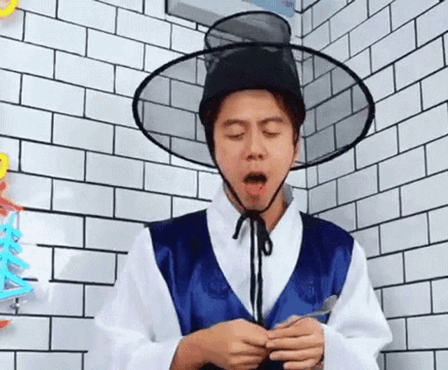 a man wearing a hat and a costume is standing in front of a brick wall .
