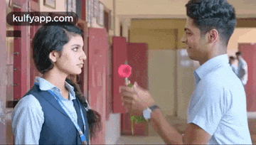 a boy is giving a girl a rose in a hallway .