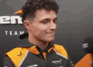 a man with curly hair wearing a black and orange jacket with the word team on it