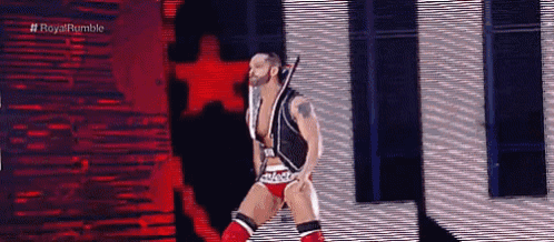 a wrestler is standing on a stage holding a sword .