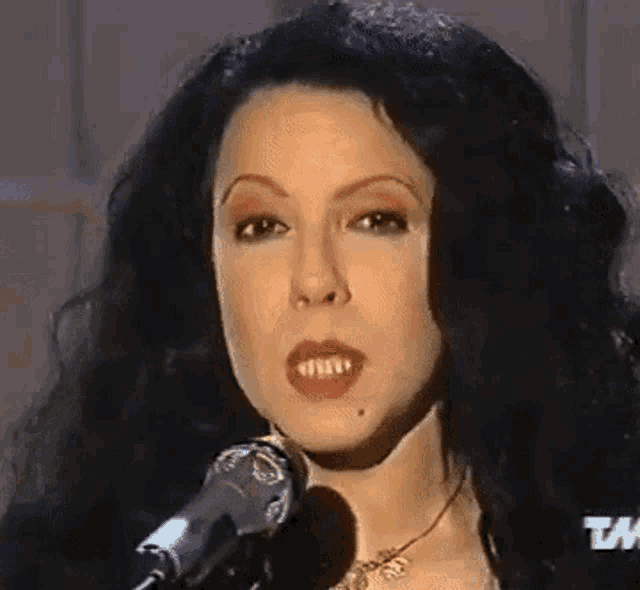 a close up of a woman singing into a microphone with a tm logo in the background .