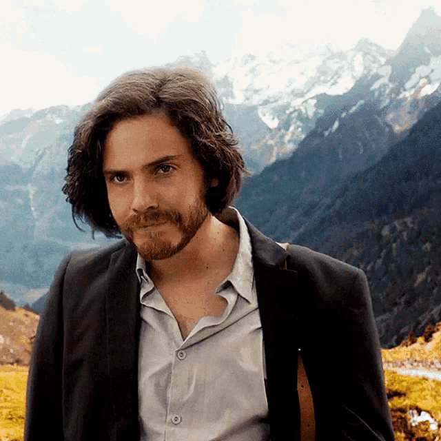 a man with long hair and a beard is standing in front of a mountain range