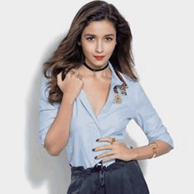 a woman wearing a choker and a blue shirt is standing in front of a wall .