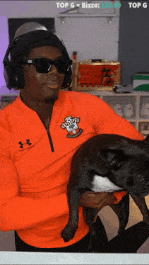 a man in an orange under armour shirt holds a small black dog