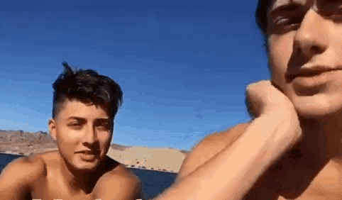 two shirtless men are sitting next to each other in front of a lake .