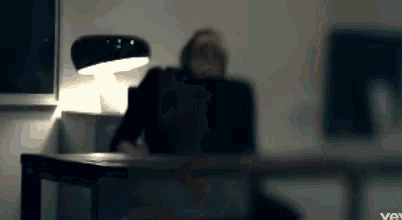 a blurred image of a person sitting at a desk with a lamp in the background