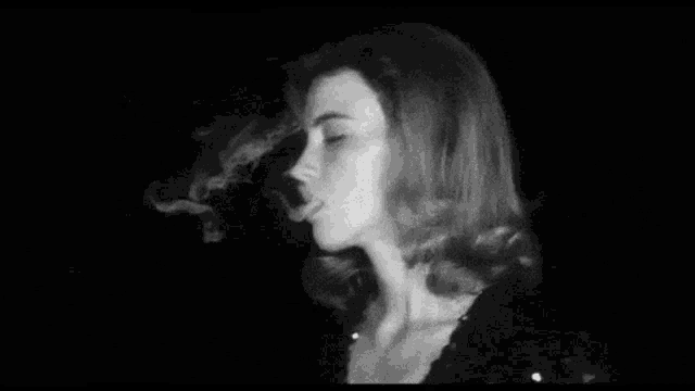 a black and white photo of a woman smoking a cigarette in the dark .