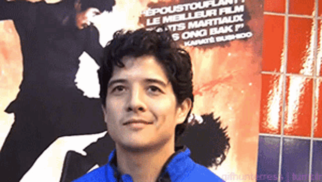 a man in a blue jacket stands in front of a poster for a martial arts film