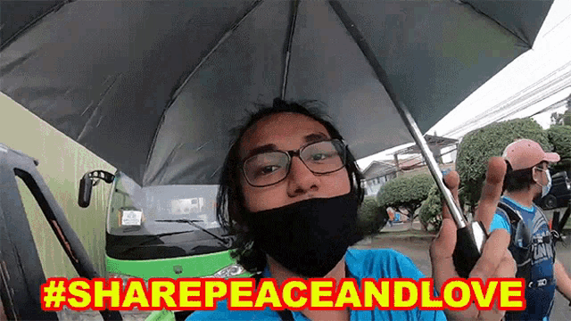 a man wearing glasses and a mask holds an umbrella with the hashtag #sharepeaceandlove above him
