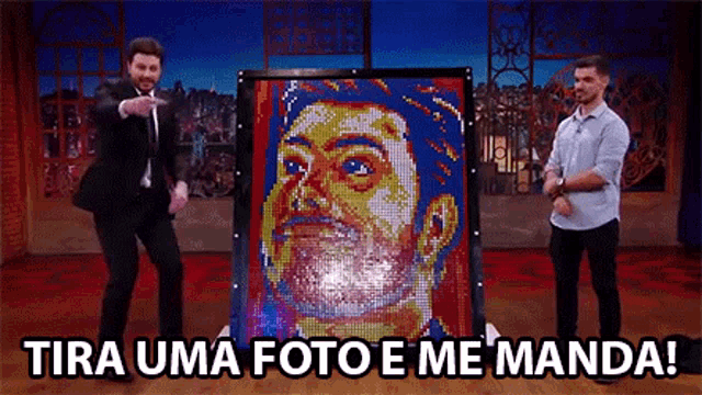 two men are standing in front of a large painting of a man 's face .