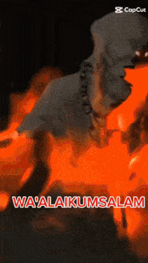 a man in a hoodie is standing in front of a fire with the words wa ' alaikumsalam written below him
