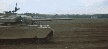 a military tank is driving through a field with smoke coming out of its cannon .