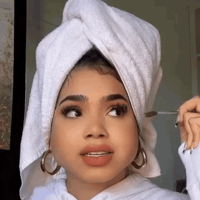 a woman with a towel around her head is applying makeup .