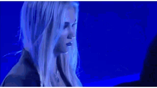 a woman with long white hair is standing in front of a blue background and looking at the camera .