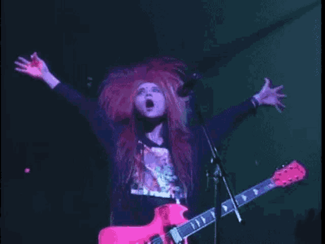 a man with long red hair is playing a pink guitar on stage .