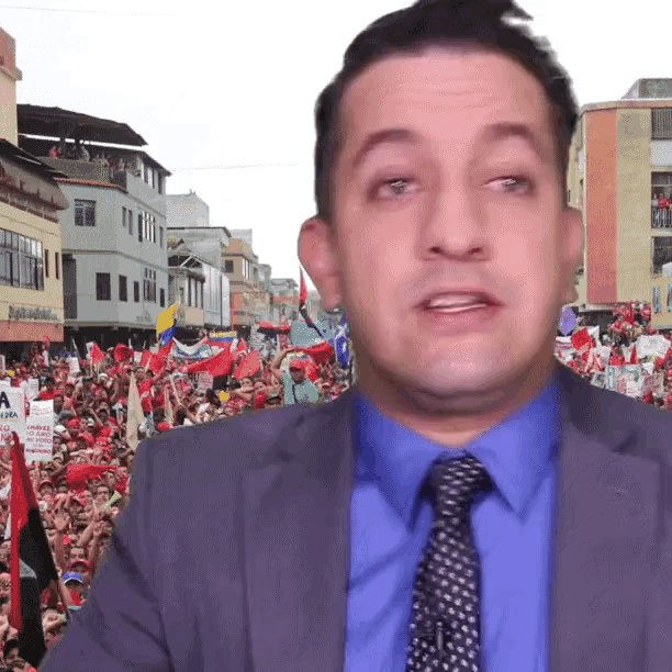 a man in a suit and tie stands in front of a crowd of people holding signs